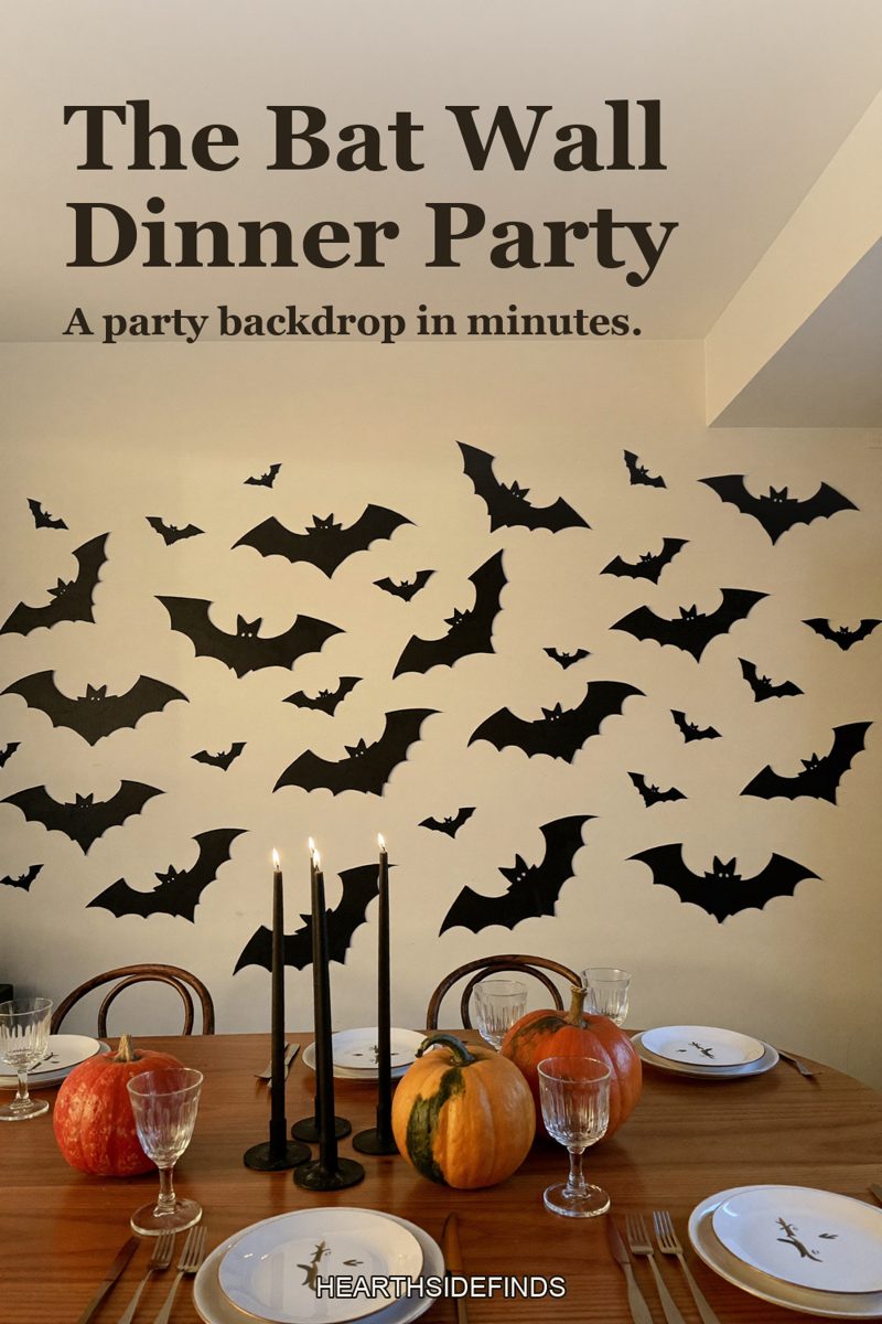 Dining table set with black candles and pumpkins in front of a pale wall covered in black paper bats.