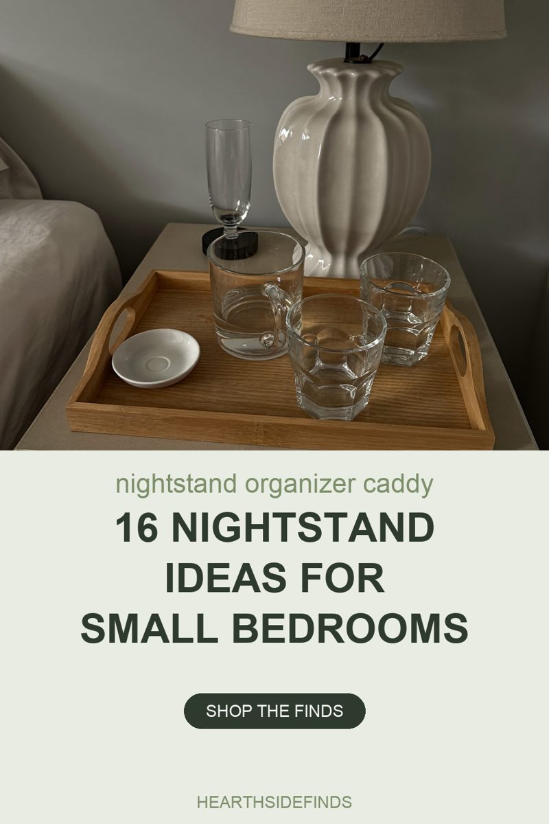 A pale wood tray with raised sides and a cut-out handle at each end sits on the flat top of a nightstand and fills the middle of the frame. Inside it are four plain clear-and-white pieces: a small white saucer at the front left, a clear glass mug with a handle behind it, and two faceted clear tumblers, one in the middle of the tray and one to the right of it. Standing on the nightstand behind the tray are a tall stemmed glass on a round black base and the fluted cream ceramic base of a lamp whose linen shade is cut off by the top of the frame. Rumpled pale bedding fills the left edge and a grey wall corner the top left. No lettering or labels anywhere.