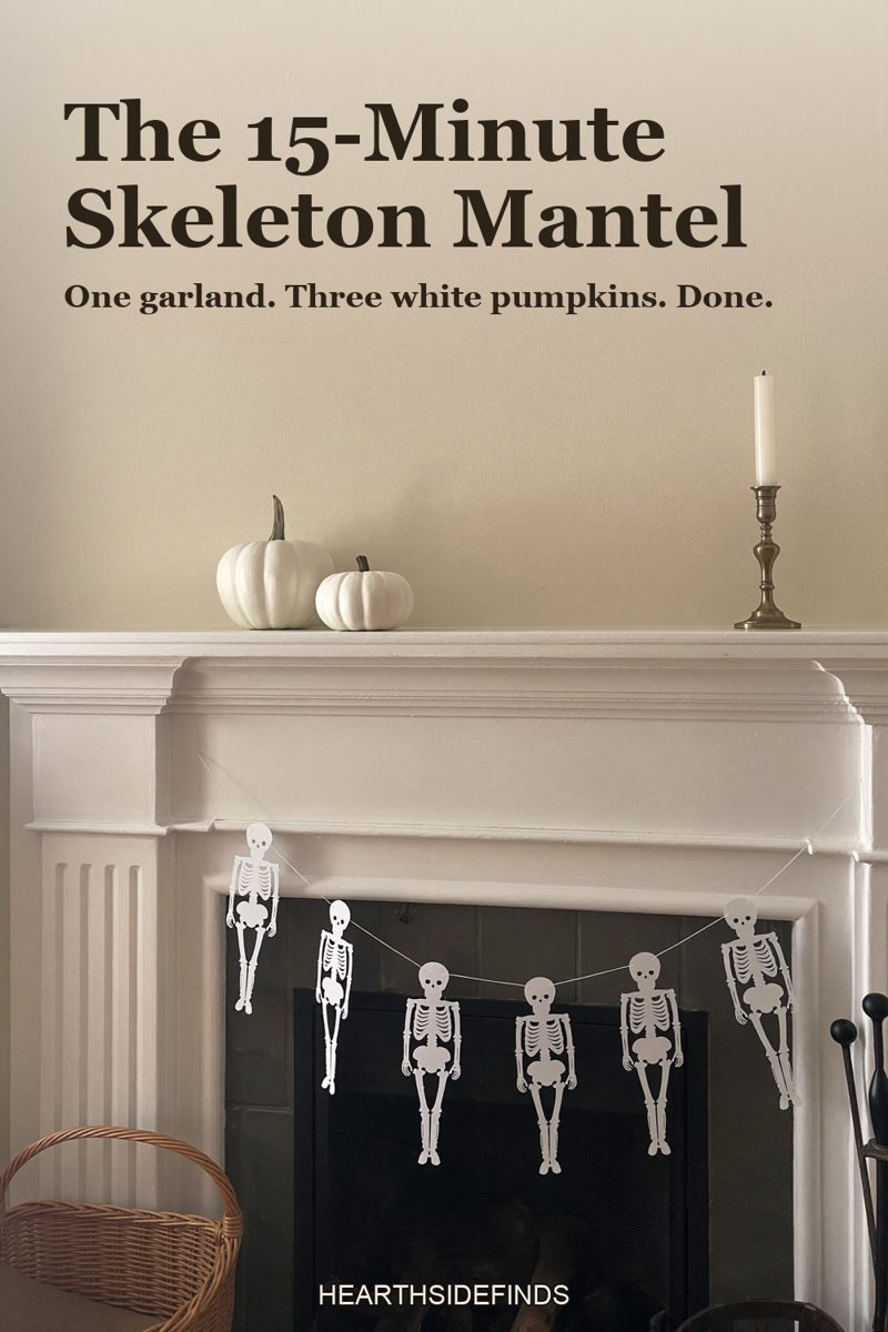 White fireplace mantel with a paper skeleton garland swagged along its edge, three white pumpkins and a brass candlestick on top, a wicker basket on the hearth.