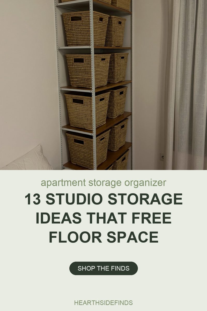 Photo of a narrow white metal shelving unit standing in the corner of a small bedroom, filled from top to bottom with woven seagrass baskets that have cut-out handle openings, two or three to each wooden shelf. The white edge of a bed and a pillow show at the lower left, a pale linen curtain hangs the full height of the right side, and a plain off-white wall fills the background.